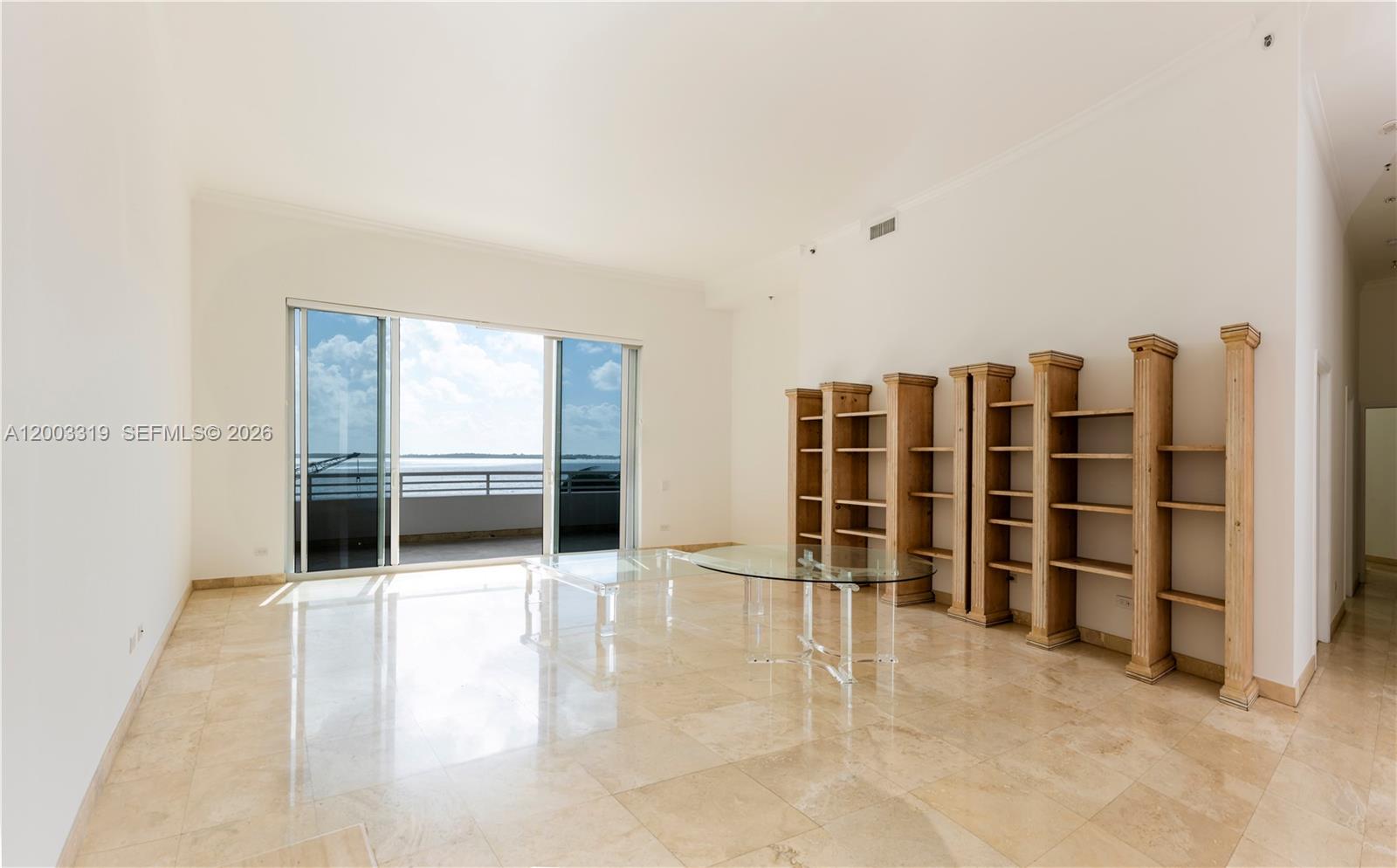 A bright living room features marble floors, built-in wooden shelving, and a balcony overlooking water — 808 Brickell Key Dr # 404, Miami FL 33131, MIAMI, FL