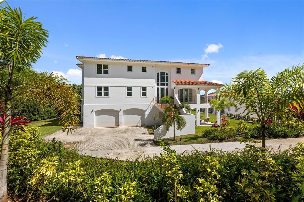 A white three-story house features a two-car garage, a balcony, and surrounding tropical landscaping — Carretera PR-175 KM. 4.0k ESMERALD LAKE PLANTATION, TRUJILLO ALTO, PR