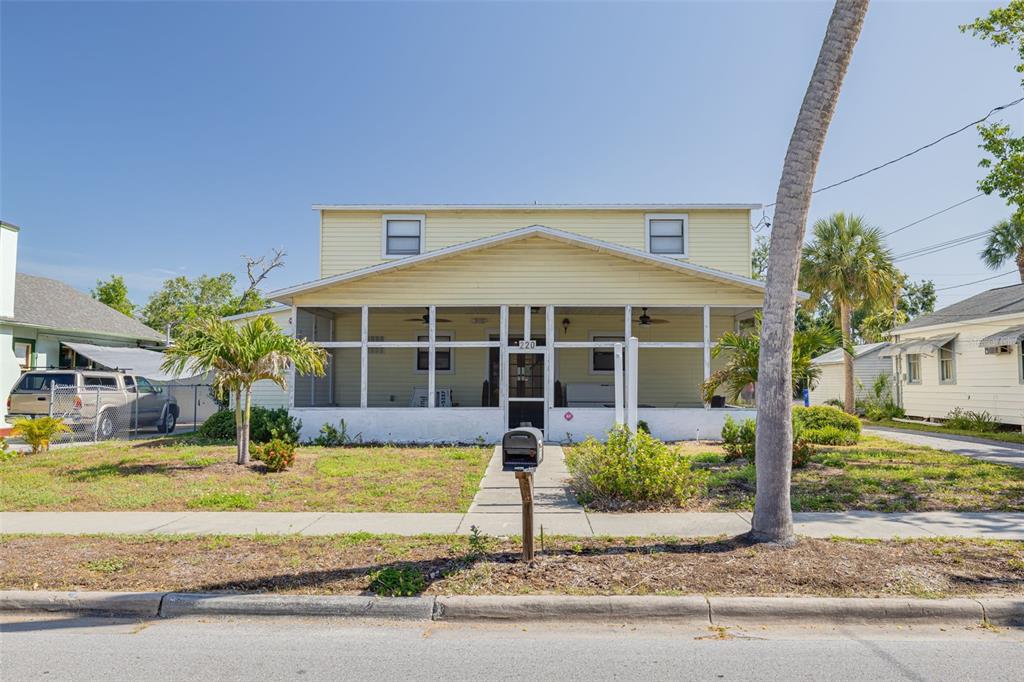 A yellow two-story house features a large screened-in front porch and a paved walkway — 220 SCOTLAND STREET, DUNEDIN, FL