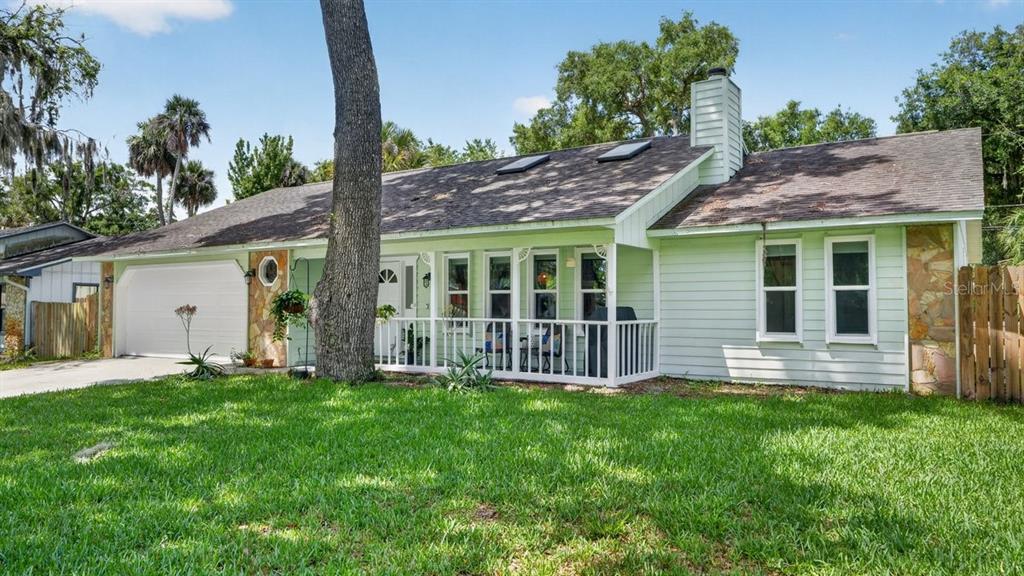 A light green single-story house with a front porch, stone accents, and a large tree — 2012 MANGO TREE DRIVE, EDGEWATER, FL