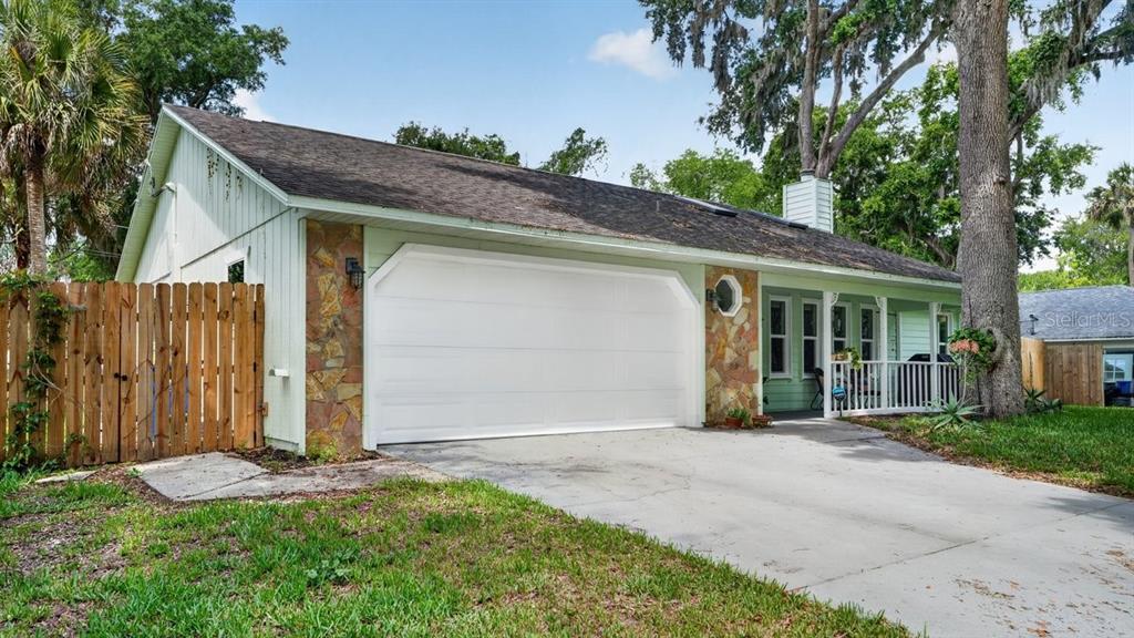 A light green house with a stone-accented garage, a covered front porch, and a wooden fence — 2012 MANGO TREE DRIVE, EDGEWATER, FL