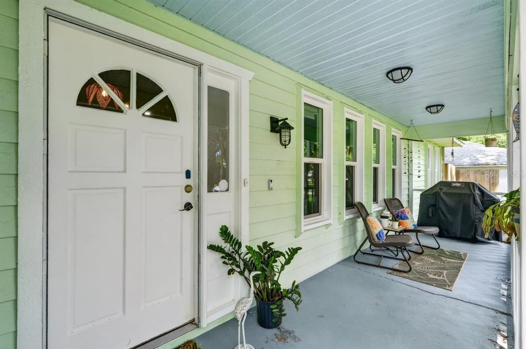A covered porch with light green siding, a white front door, and outdoor seating — 2012 MANGO TREE DRIVE, EDGEWATER, FL