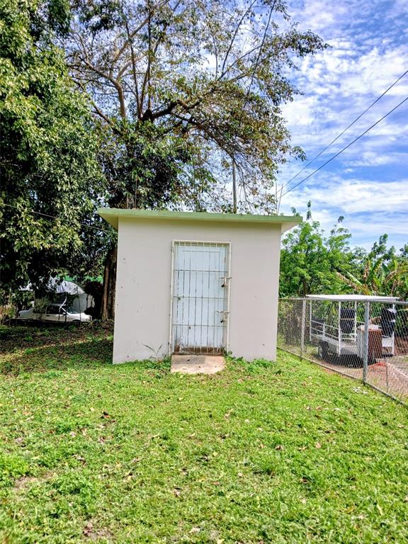 A small, light-colored concrete shed with a white metal security door stands in a yard — 372 SECTOR COTUY, YAUCO, PR