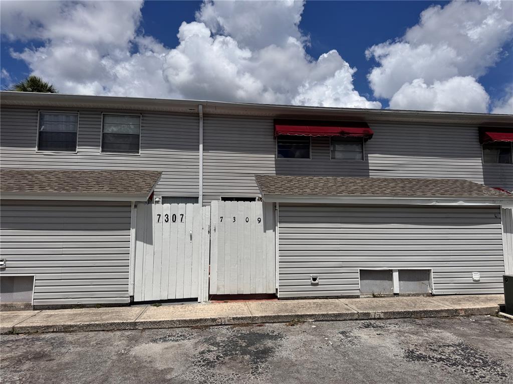 The exterior of a two-story townhouse features gray siding, white privacy gates, and red awnings — 7309 JACKSON SPRINGS ROAD, TAMPA, FL