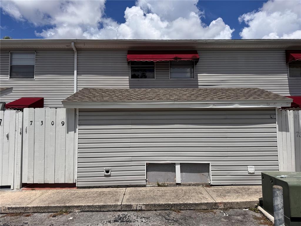 The exterior of a two-story townhouse features gray horizontal siding and red window awnings — 7309 JACKSON SPRINGS ROAD, TAMPA, FL