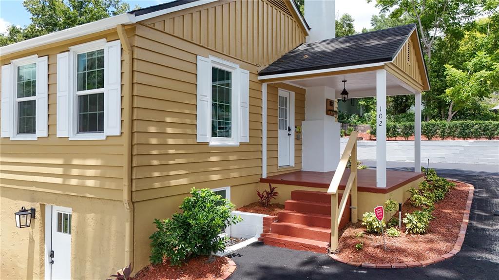 A tan house with a covered porch, red steps, and a lower-level white door — 102 N CLAYTON STREET, MOUNT DORA, FL