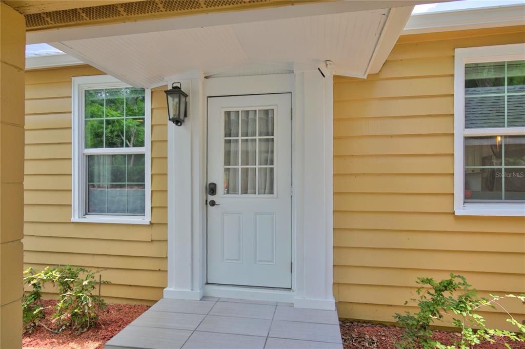 A white front door with a window sits between two windows on a yellow house — 102 N CLAYTON STREET, MOUNT DORA, FL