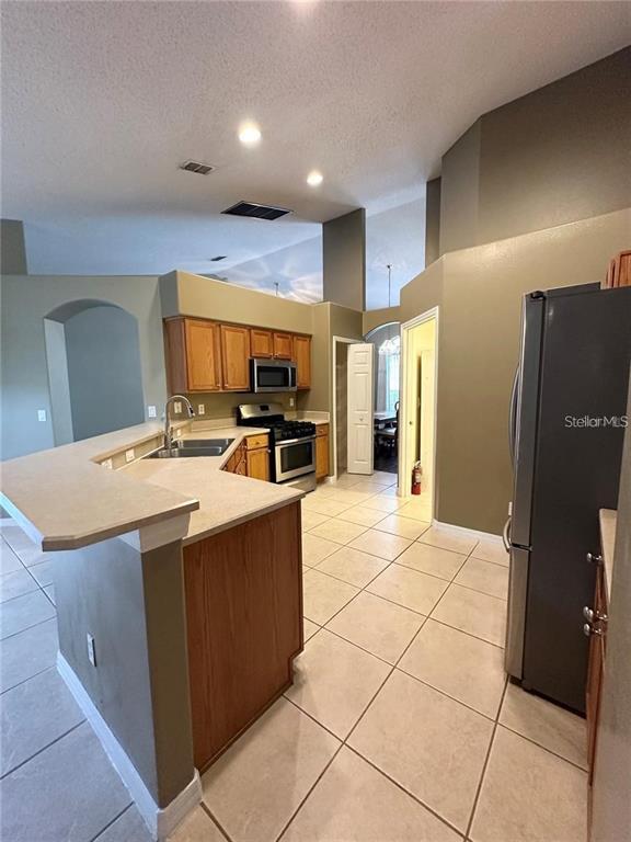 A kitchen features light-colored countertops, wood cabinets, stainless steel appliances, and tile flooring — 16016 BLOSSOM HILL LOOP, CLERMONT, FL