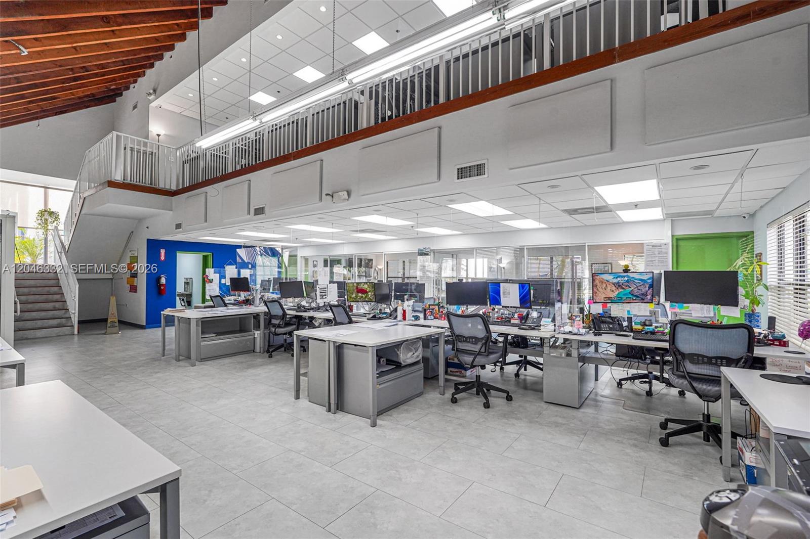 An open-plan office features multiple workstations, a tiled floor, and a mezzanine level with stairs — 1400 NW 79th Ave, Doral FL 33126, DORAL, FL