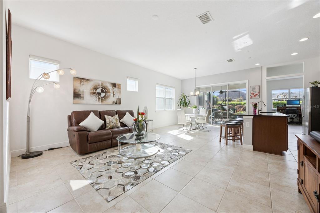 An open-concept living room and kitchen featuring tile floors, a brown leather sofa, and sliding doors — 4902 W FOUNTAINWOOD DRIVE, ST CLOUD, FL
