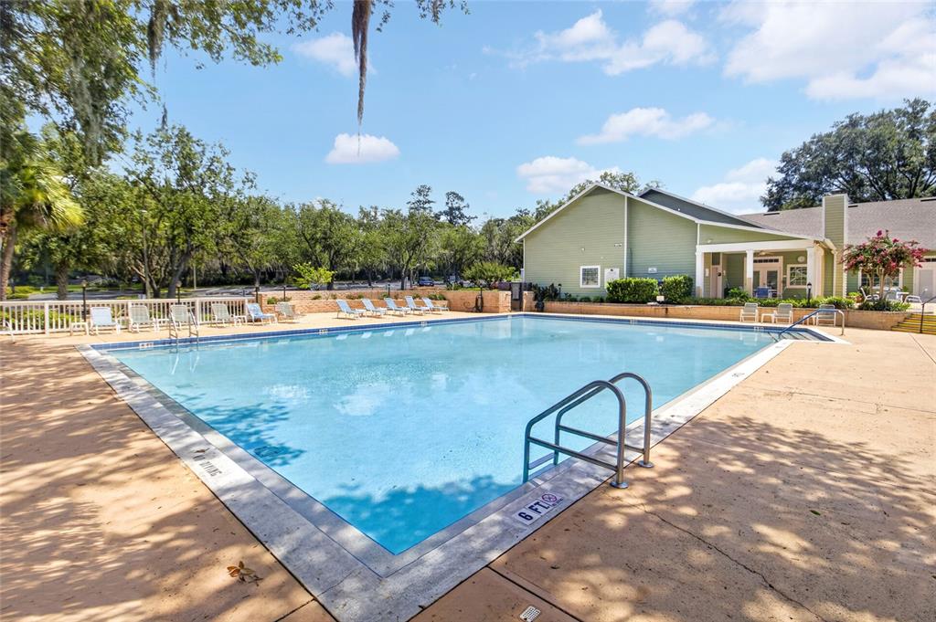 A rectangular swimming pool sits in front of a green building with lounge chairs nearby — 10549 NW 32ND ROAD, GAINESVILLE, FL