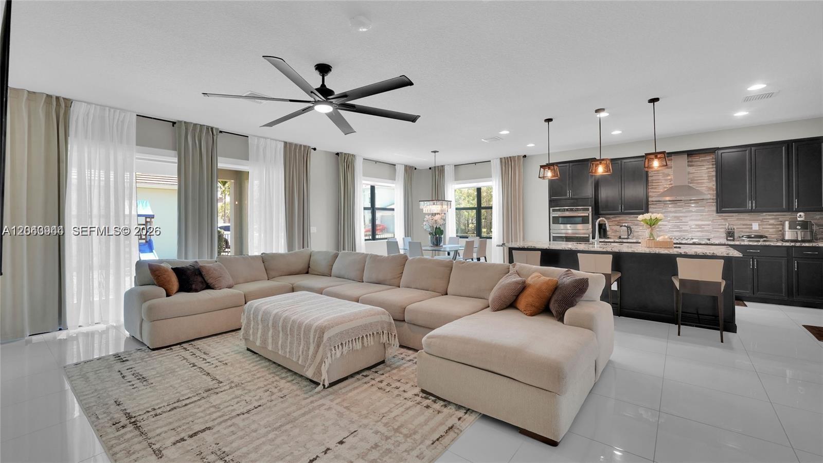 A modern open-concept living room features a large sectional sofa, kitchen island, and tile flooring — 7349 Stella Ln, Lake Worth FL 33463, LAKE WORTH, FL