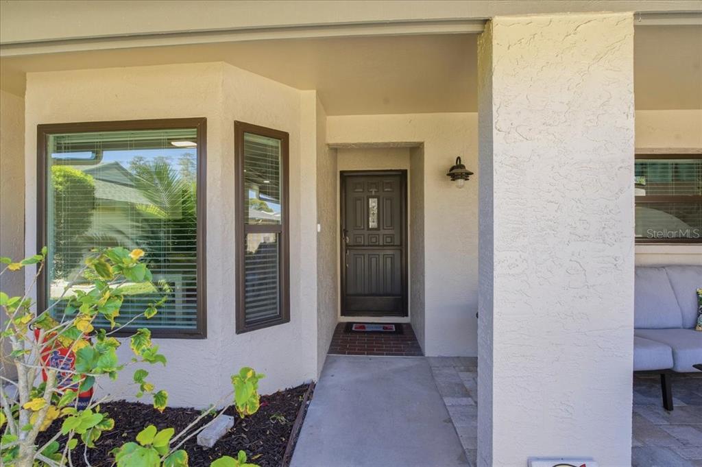 A covered front entryway features a dark paneled door, a window, and a brick floor — 3272 LORI LANE, NEW PORT RICHEY, FL