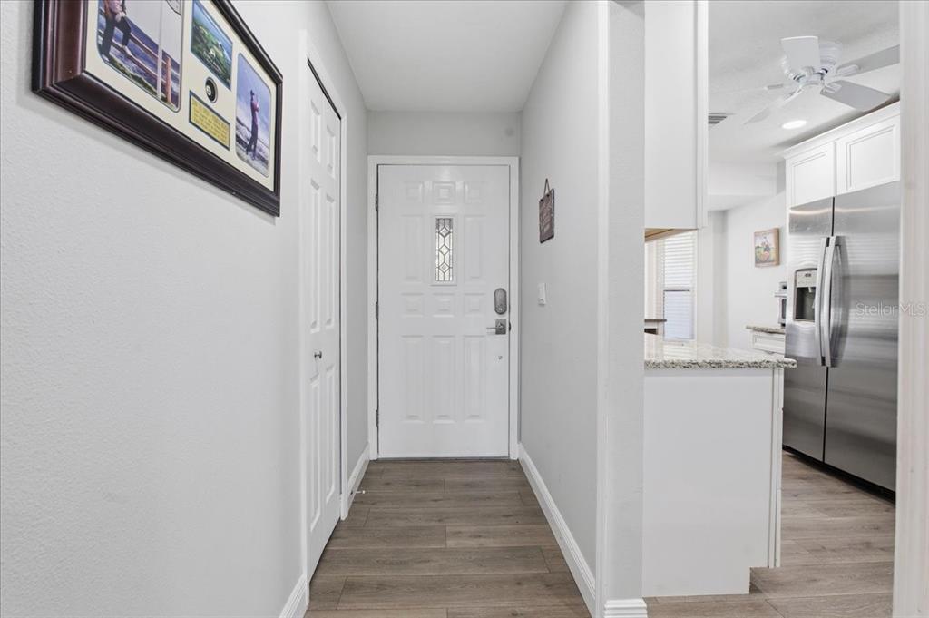 An entryway with wood-look flooring leads to a white front door and an adjacent kitchen — 3272 LORI LANE, NEW PORT RICHEY, FL