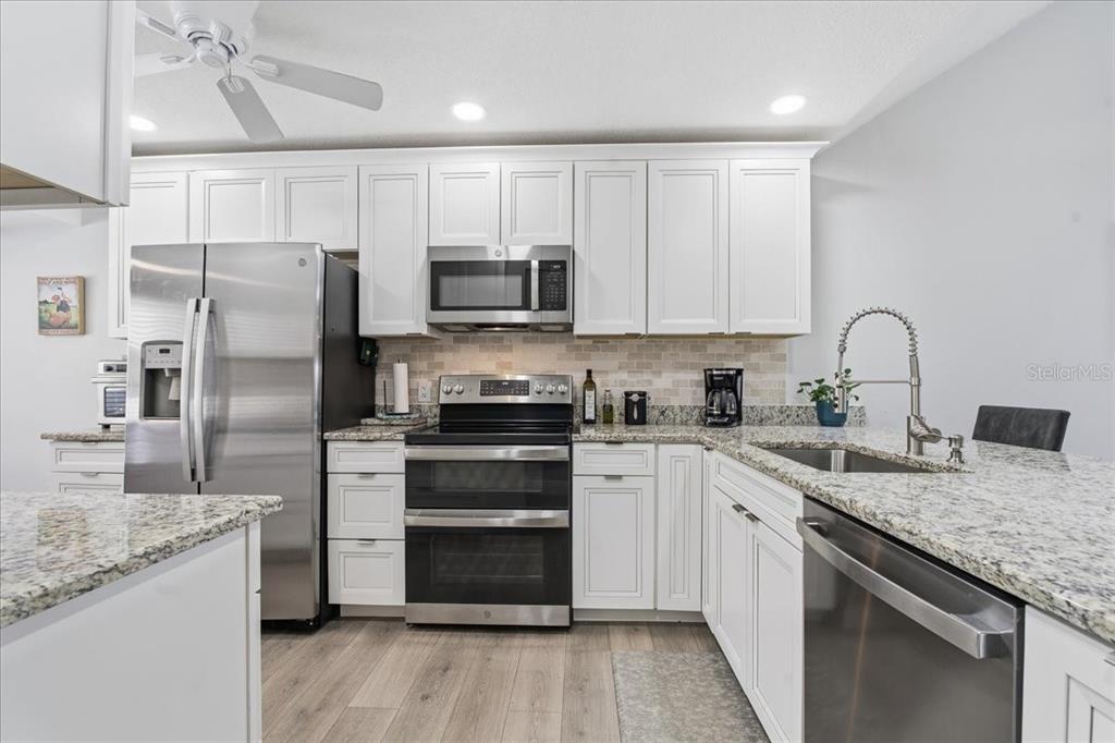 A kitchen features white cabinets, stainless steel appliances, granite countertops, and light wood-look flooring — 3272 LORI LANE, NEW PORT RICHEY, FL