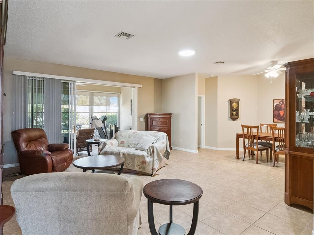 A living room and dining area with tile floors, neutral walls, and sliding glass doors — 20639 PRINCE RANIER PLACE, LEESBURG, FL