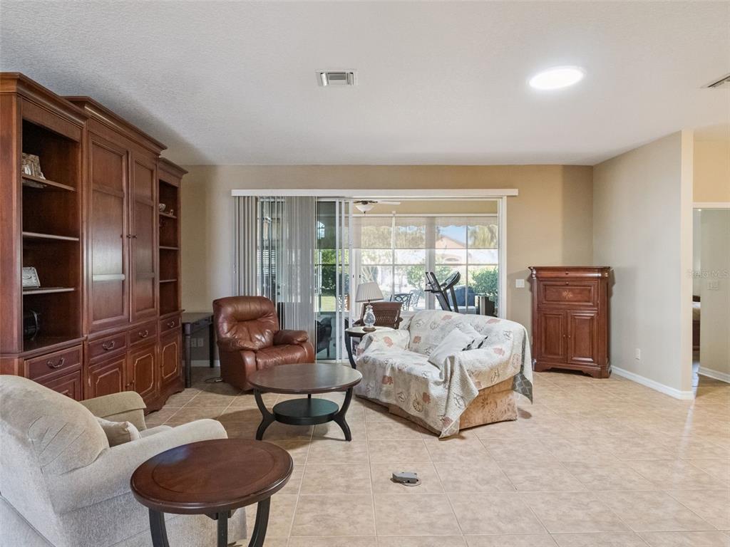 A living room features tile flooring, a large wooden wall unit, and sliding glass patio doors — 20639 PRINCE RANIER PLACE, LEESBURG, FL