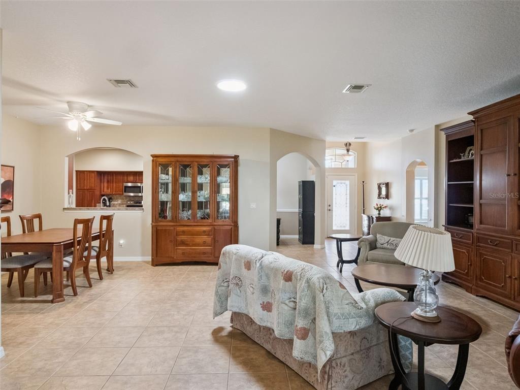 An open-concept living and dining area features tile flooring, wood cabinetry, and arched doorways — 20639 PRINCE RANIER PLACE, LEESBURG, FL