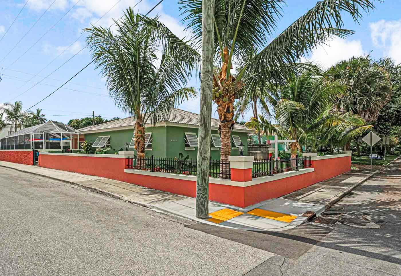A green house with a red perimeter wall and palm trees sits on a corner lot — 532 N Palmway, FL 33460, FL