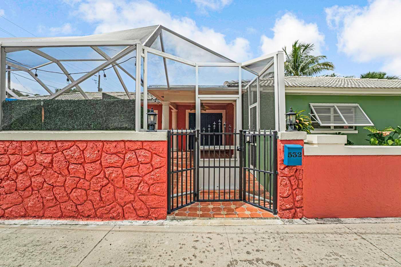 A gated entrance leads to a screened-in courtyard in front of a house with red stone walls — 532 N Palmway, FL 33460, FL