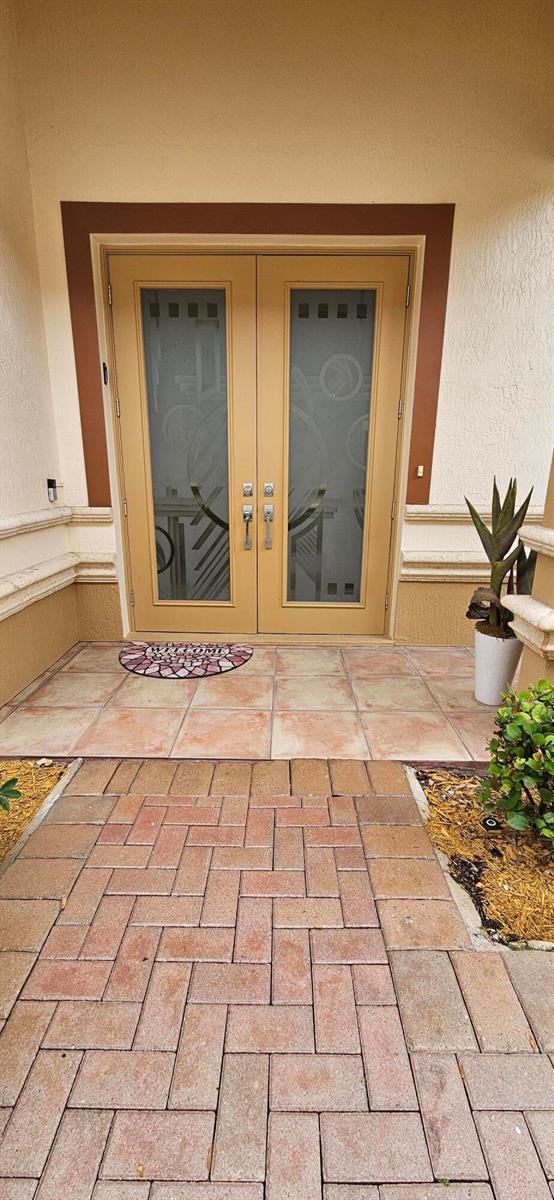 A paved walkway leads to a double-door entryway with frosted glass panels and tile flooring — 16117 Emerald Estates Drive, Weston FL 33331, WESTON, FL