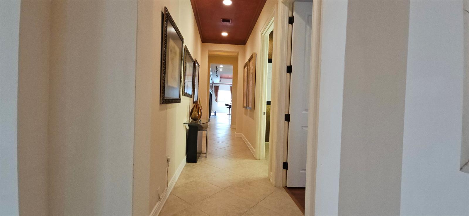 A hallway with tile flooring, a dark red ceiling, and framed wall art — 16117 Emerald Estates Drive, Weston FL 33331, WESTON, FL