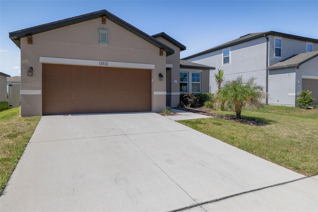 A tan single-story house features a two-car garage, a concrete driveway, and a small palm tree — 13512 PALMERA VISTA DRIVE, RIVERVIEW, FL