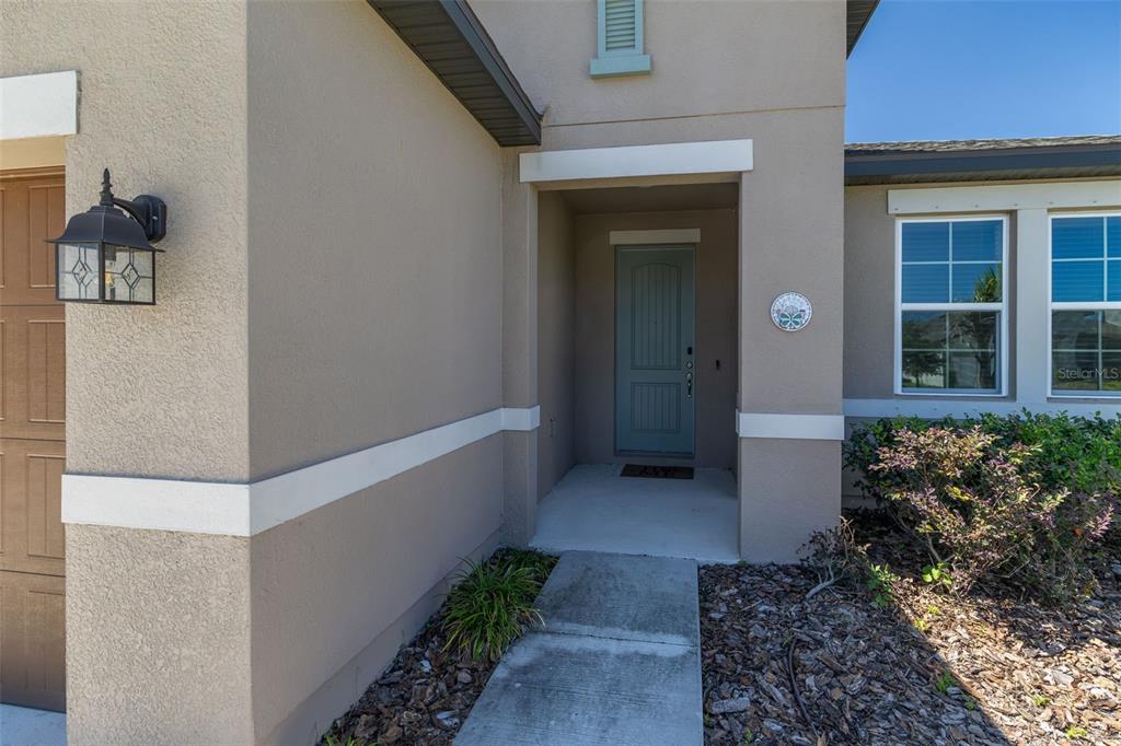 A tan house exterior features a recessed entryway with a blue door and concrete walkway — 13512 PALMERA VISTA DRIVE, RIVERVIEW, FL