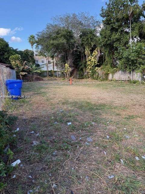 A vacant, grassy lot with a blue trash bin and surrounding trees and fences — 1121 NW 2nd St, Miami FL 33128, MIAMI, FL