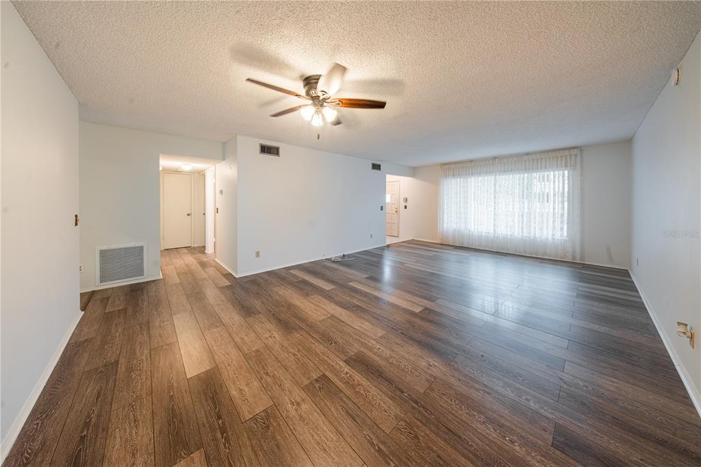 A spacious living room features wood-look flooring, a ceiling fan, and a large window — 2170 AMERICUS BOULEVARD N UNIT 44, CLEARWATER, FL