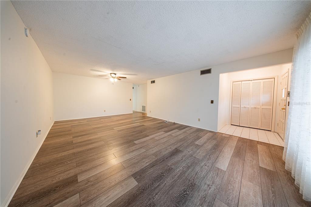 An empty living room features wood-look flooring, white walls, a ceiling fan, and a closet — 2170 AMERICUS BOULEVARD N UNIT 44, CLEARWATER, FL
