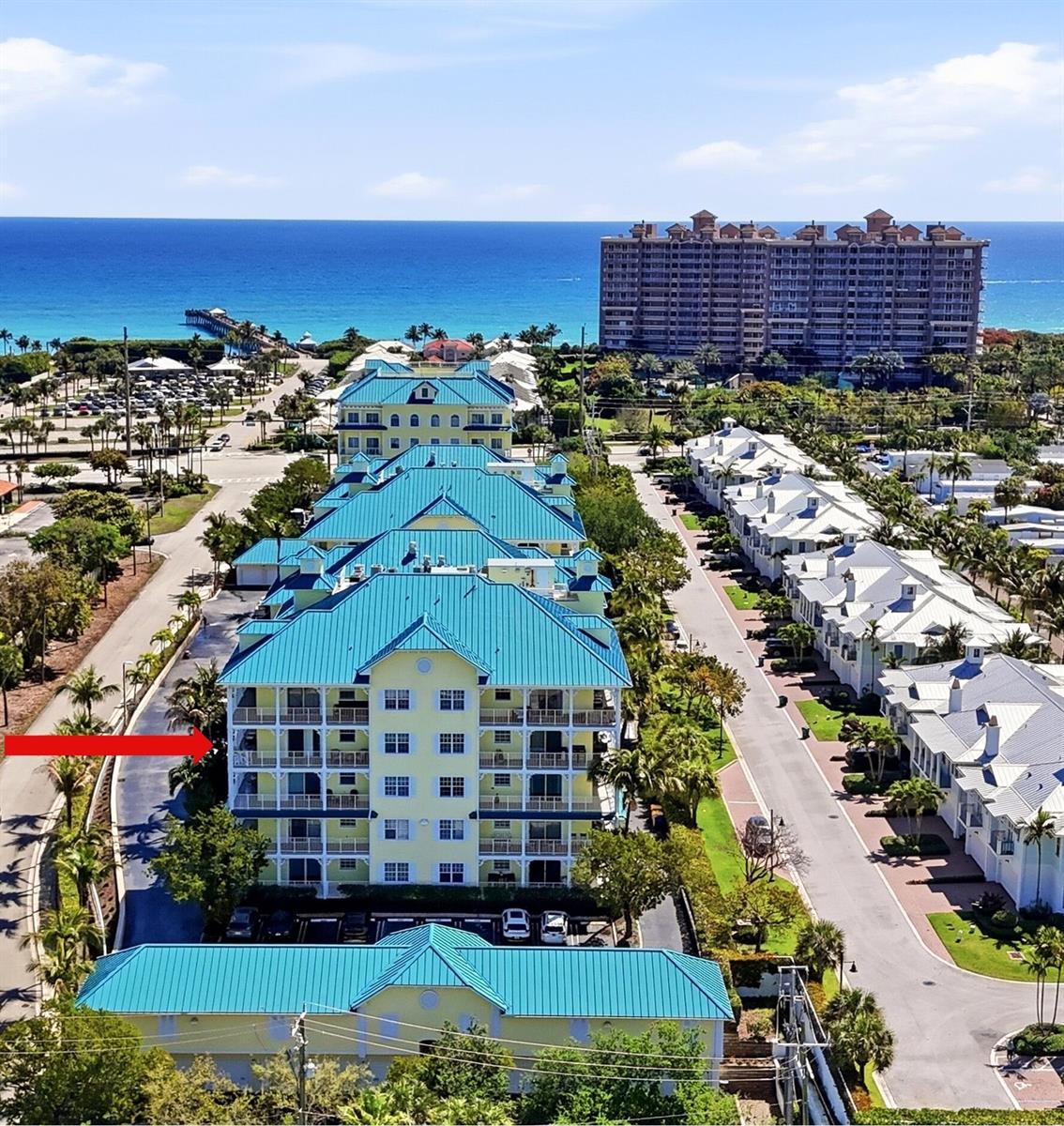 An aerial view shows a multi-story yellow building with a blue roof near the ocean — 810 Juno Ocean Walk # 402, Juno Beach FL 33408, JUNO BEACH, FL