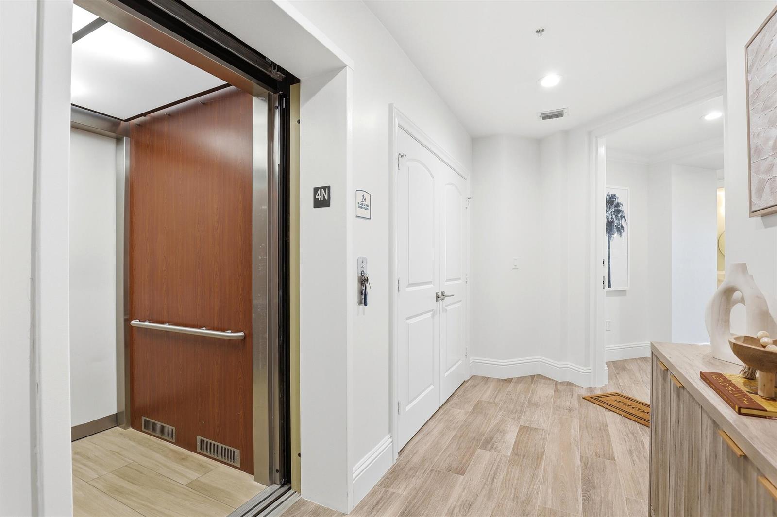 An elevator opens into a hallway with white walls, wood-look flooring, and double doors — 810 Juno Ocean Walk # 402, Juno Beach FL 33408, JUNO BEACH, FL
