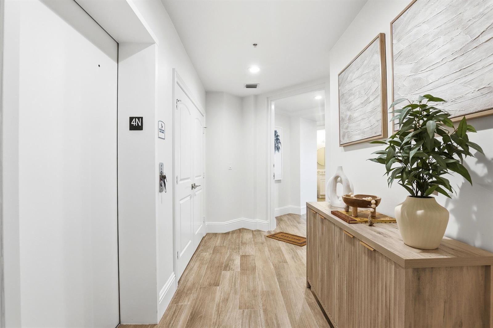 A bright hallway features wood-look tile flooring, a wooden console table, and white doors — 810 Juno Ocean Walk # 402, Juno Beach FL 33408, JUNO BEACH, FL