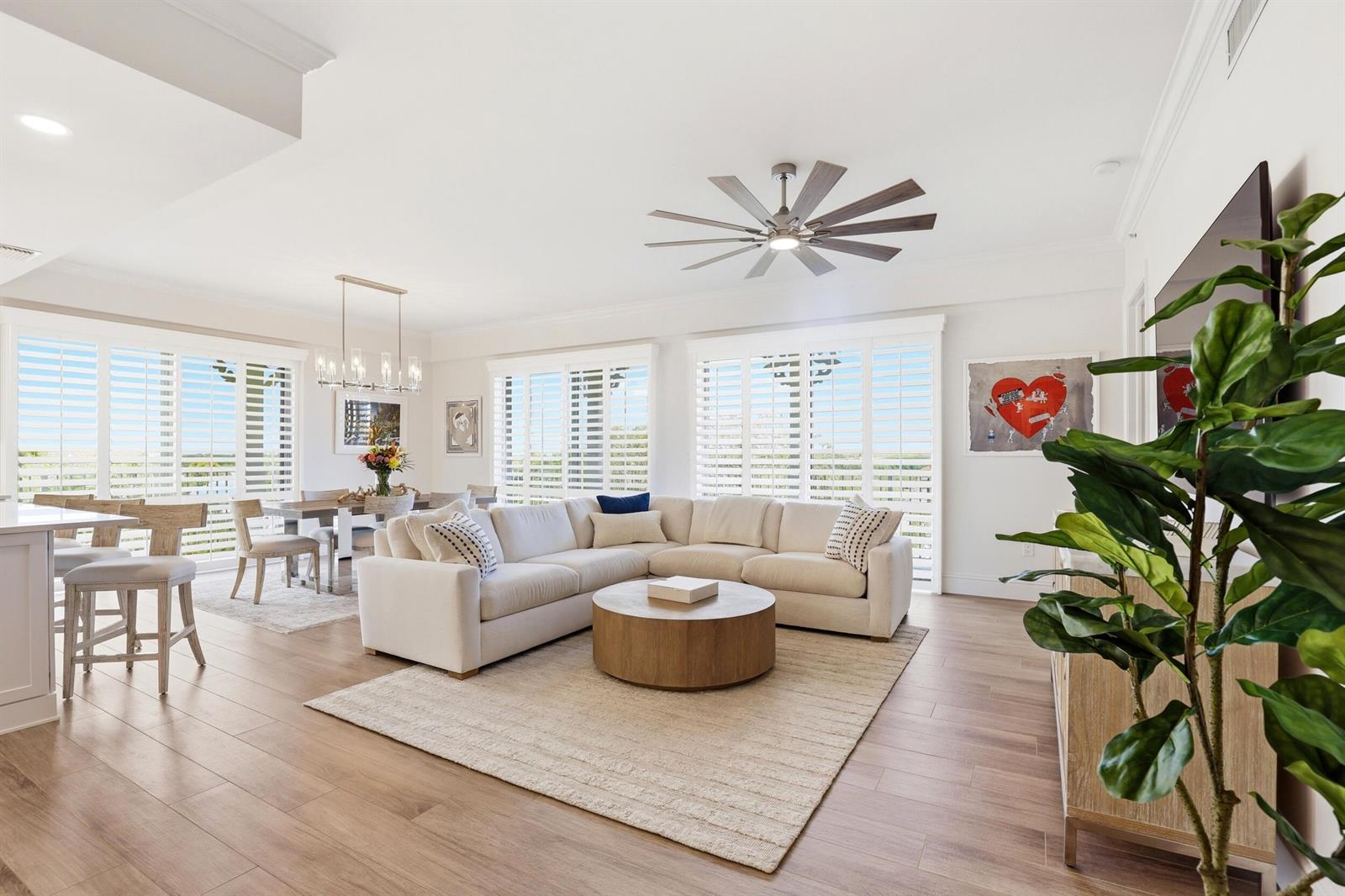 A bright, open-concept living and dining area features a large sectional sofa and wood flooring — 810 Juno Ocean Walk # 402, Juno Beach FL 33408, JUNO BEACH, FL
