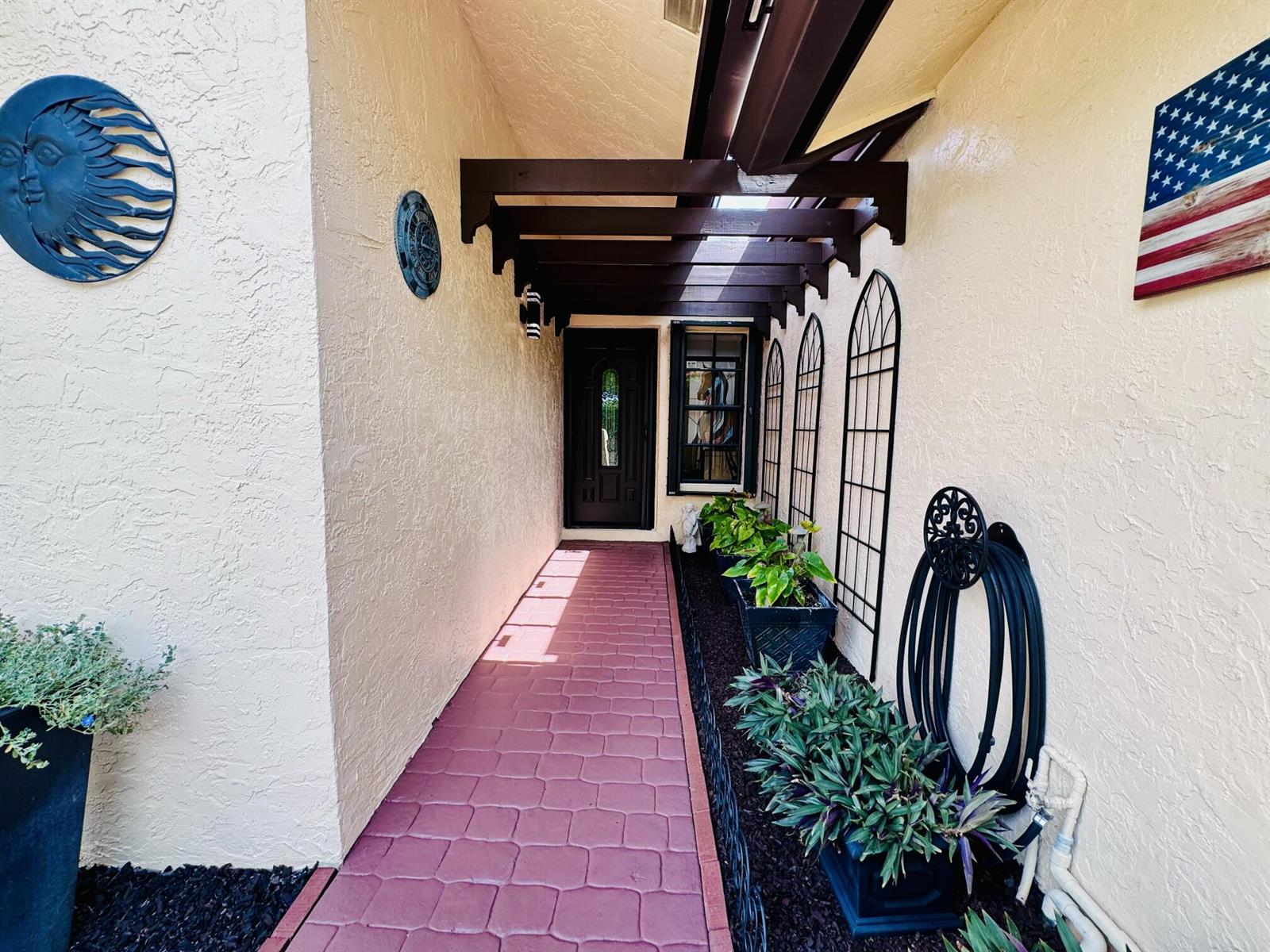 A covered walkway leads to a dark front door, flanked by planters and wall decor — 5157 Magellan Way E, Delray Beach FL 33484, DELRAY BEACH, FL