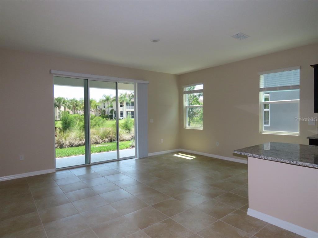 An empty room with beige tile flooring, sliding glass doors, and windows overlooking greenery — 8725 DAYDREAM STREET, SARASOTA, FL