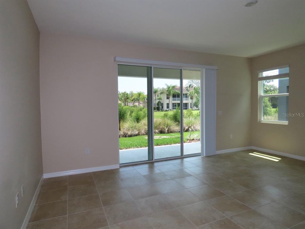 An empty room with beige walls, tile flooring, sliding glass doors, and a side window — 8725 DAYDREAM STREET, SARASOTA, FL