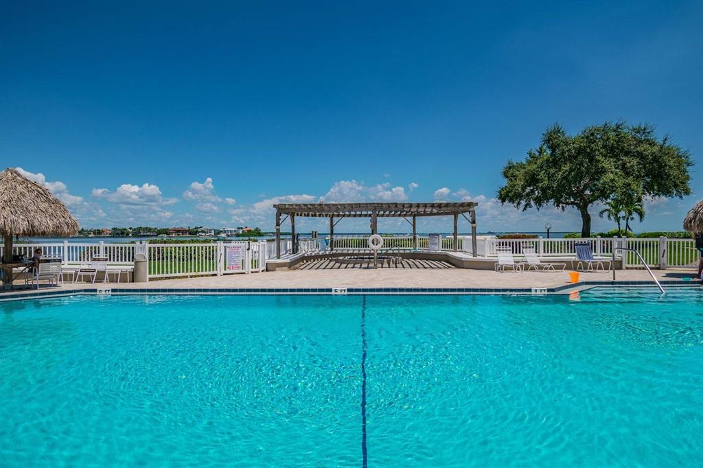A swimming pool sits in front of a wooden pergola with a white fence beyond — 6104 PALMA DEL MAR BOULEVARD S UNIT 604, ST PETERSBURG, FL