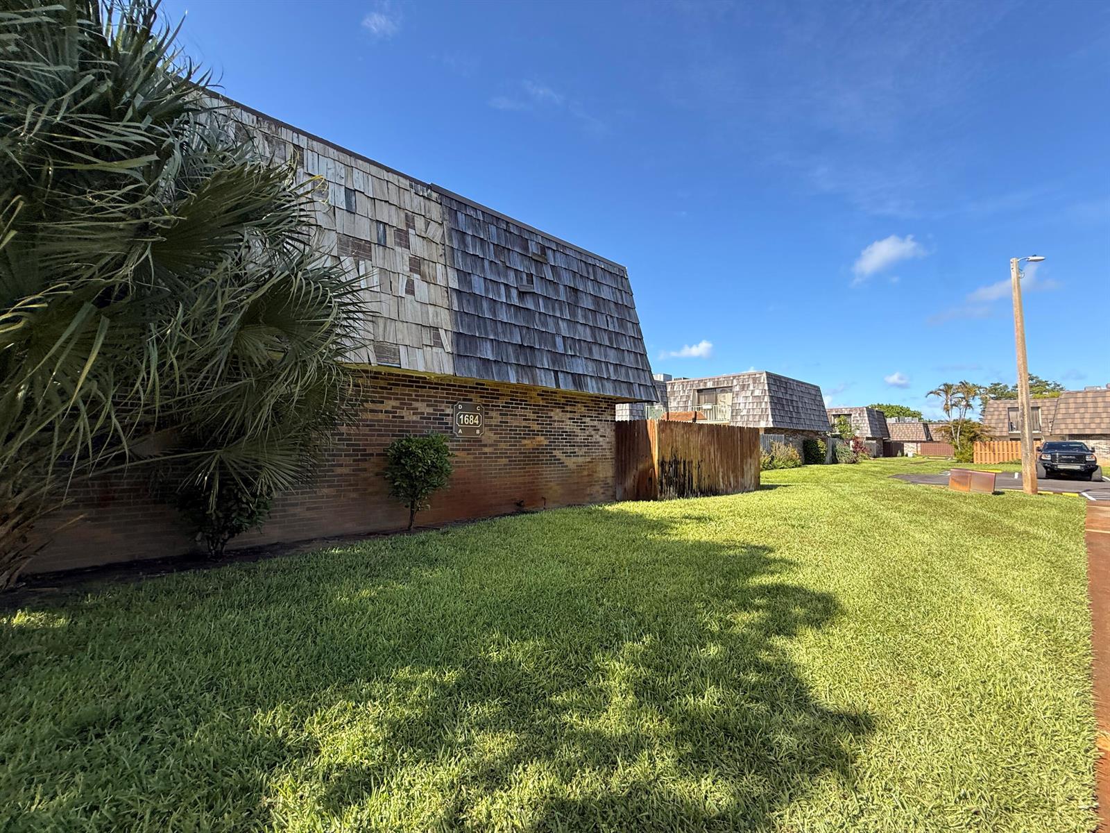 A brick apartment building with a shingled mansard roof sits beside a grassy lawn — 1684 Forest Lakes Circle # A, West Palm Beach FL 33406, WEST PALM BEACH, FL
