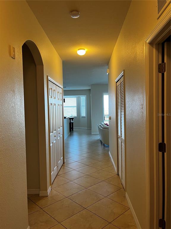 A hallway with tiled floors leads toward a living area with a view of windows — 7911 GRAND ESTUARY TRAIL UNIT 406, BRADENTON, FL