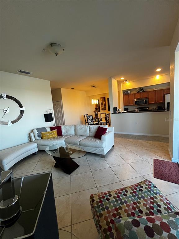 A living room with a white sectional sofa, glass coffee table, and an open kitchen — 7911 GRAND ESTUARY TRAIL UNIT 406, BRADENTON, FL