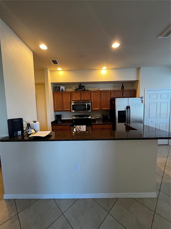 A kitchen features wood cabinets, granite countertops, stainless steel appliances, and a breakfast bar — 7911 GRAND ESTUARY TRAIL UNIT 406, BRADENTON, FL