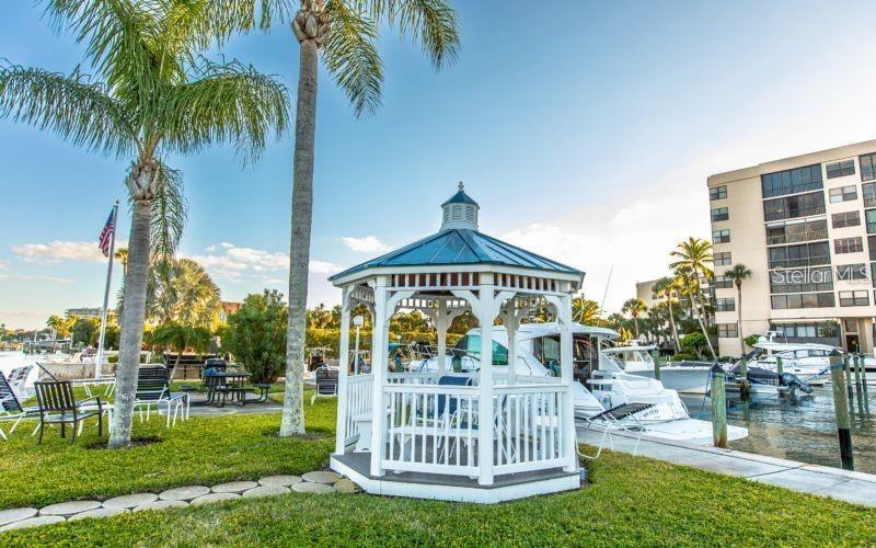 A white gazebo sits on a grassy lawn near a marina with boats and buildings — 5855 MIDNIGHT PASS ROAD UNIT 333, SARASOTA, FL