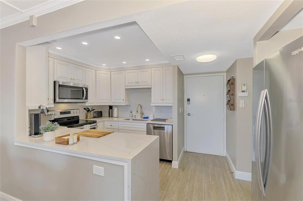 A kitchen features white cabinets, stainless steel appliances, and a quartz countertop peninsula — 5855 MIDNIGHT PASS ROAD UNIT 333, SARASOTA, FL