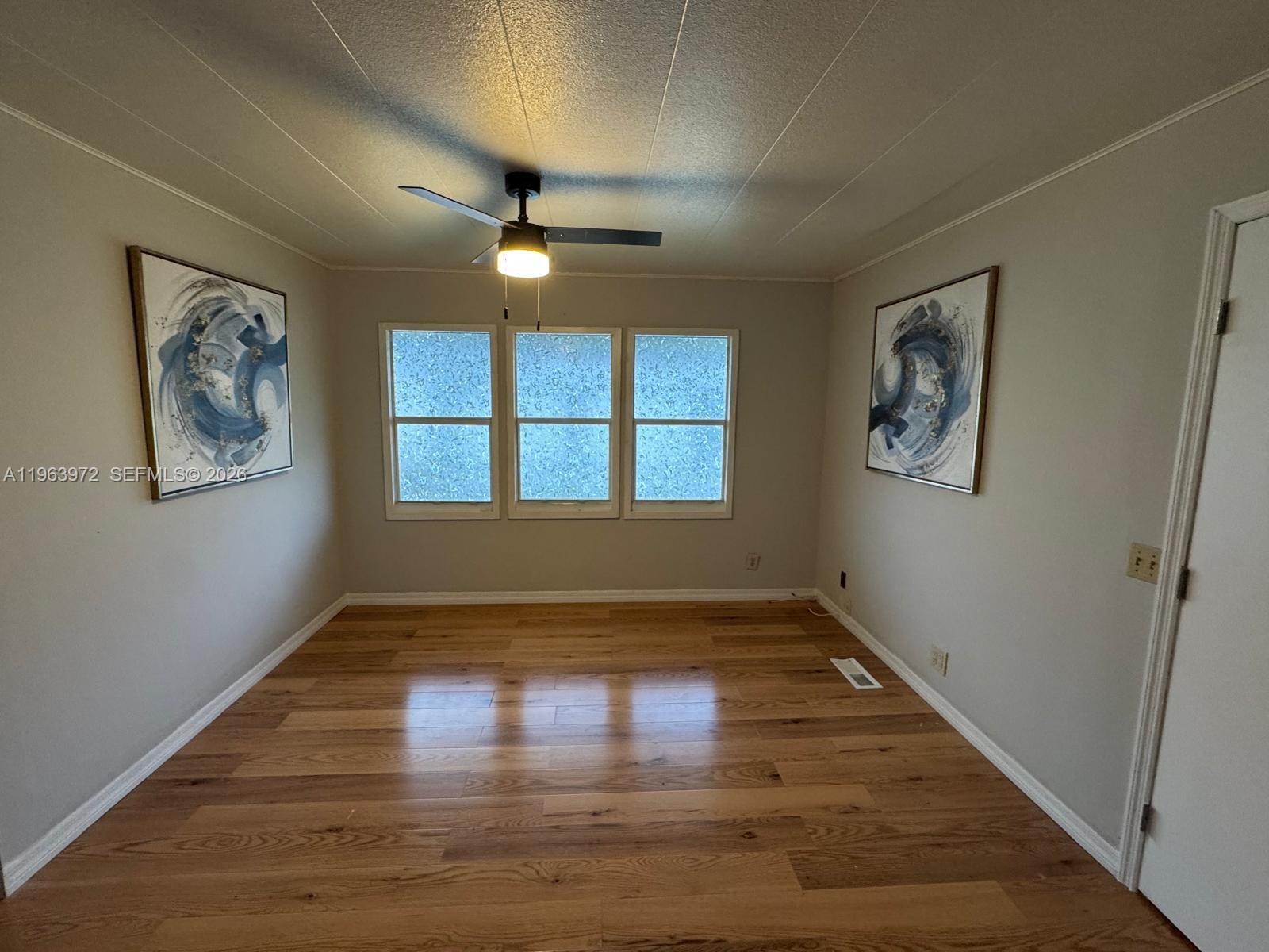 An empty room features light wood flooring, a ceiling fan, and two abstract wall paintings — 1721 SW 84th Ave, Davie FL 33324, DAVIE, FL