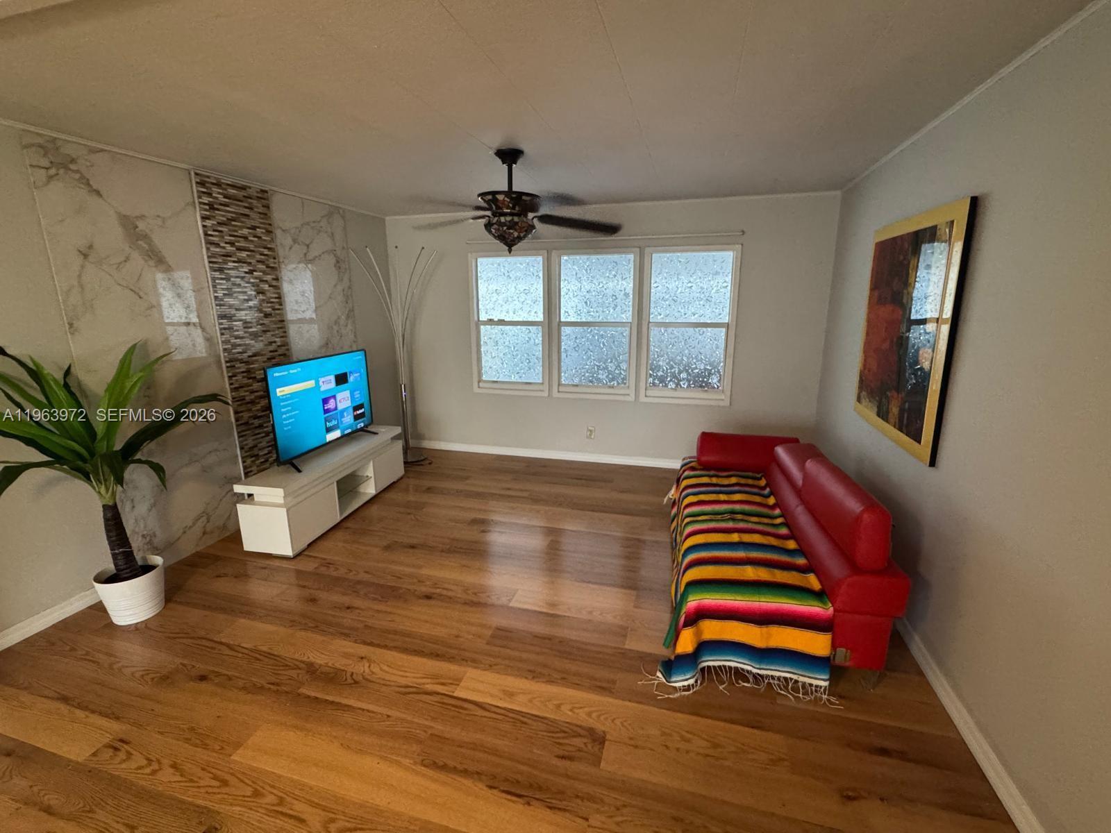 A living room features wood flooring, a red sofa, a television, and a ceiling fan — 1721 SW 84th Ave, Davie FL 33324, DAVIE, FL