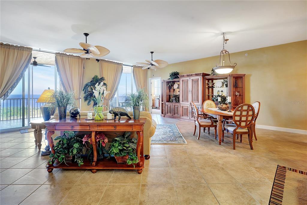 A spacious living and dining area features tile floors, wooden furniture, and floor-to-ceiling windows — 3191 MATECUMBE KEY ROAD UNIT 704, PUNTA GORDA, FL