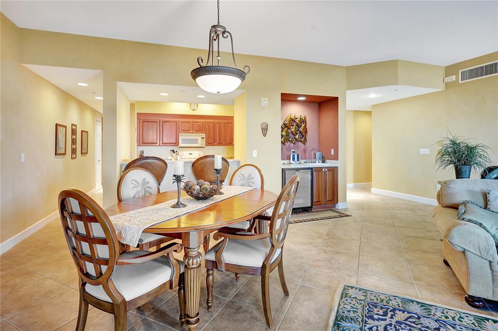 A dining area with a wooden table and chairs sits adjacent to a kitchen and bar — 3191 MATECUMBE KEY ROAD UNIT 704, PUNTA GORDA, FL