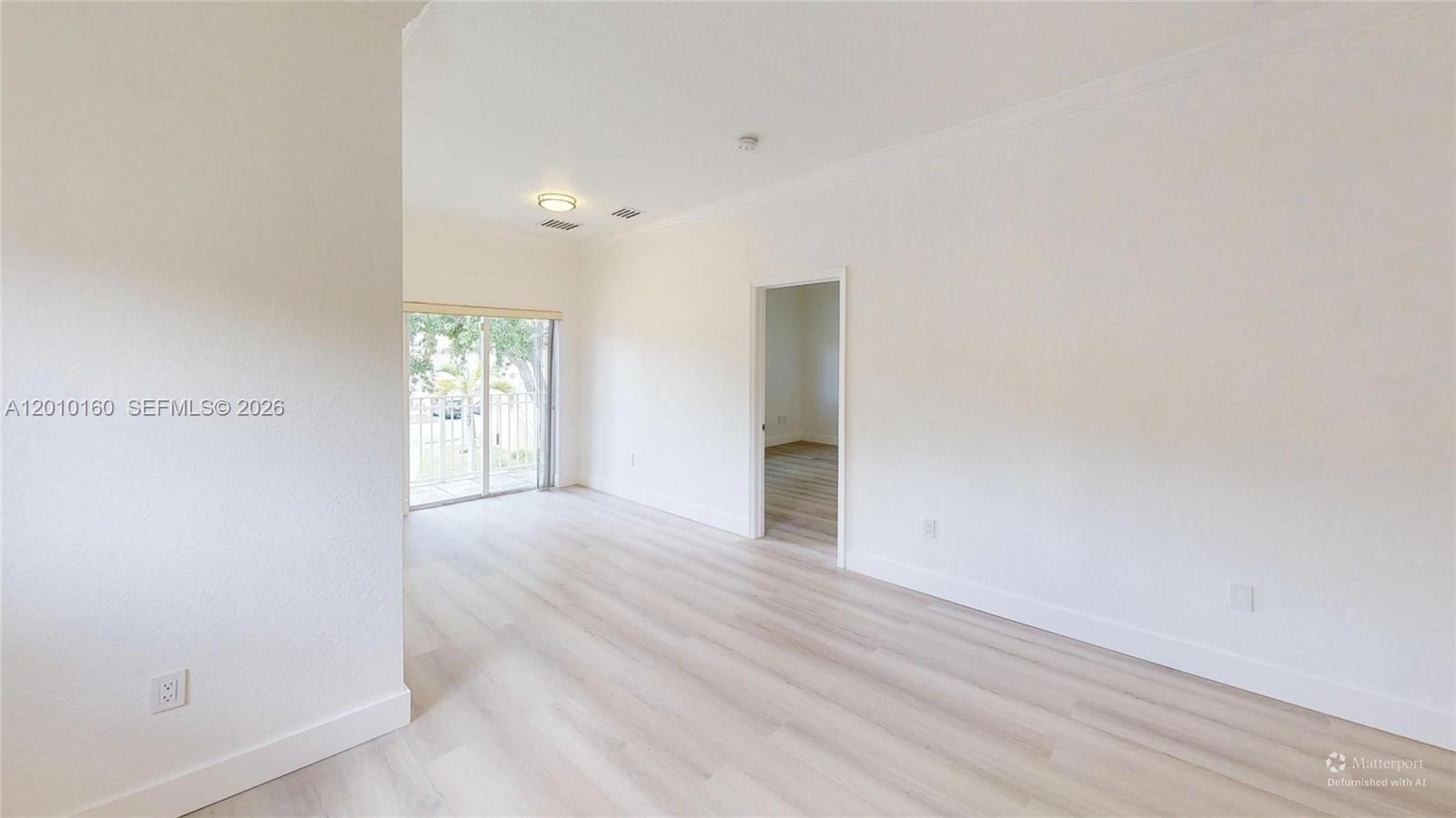 An empty room features light-colored wood-look flooring, white walls, and a sliding glass door — 372 NE 26th Pl # 201, Homestead FL 33033, HOMESTEAD, FL